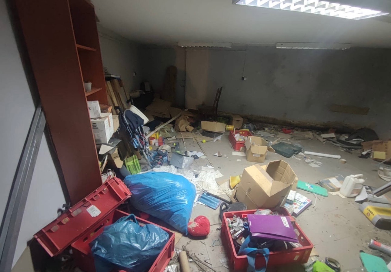 Zagracone pomieszczenie w trakcie opróżniania: worki na śmieci, kartony, skrzynki, meble. Widoczny surowy beton na ścianach i suficie z lampami.