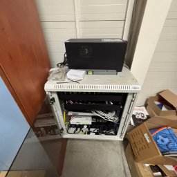cenIT Andrzej Cendrowski - Szafa rack z zainstalowanymi urządzeniami sieciowymi i zasilaczem UPS na górze, widok z góry, obok kartony. Element sieci komputerowej w pomieszczeniu.