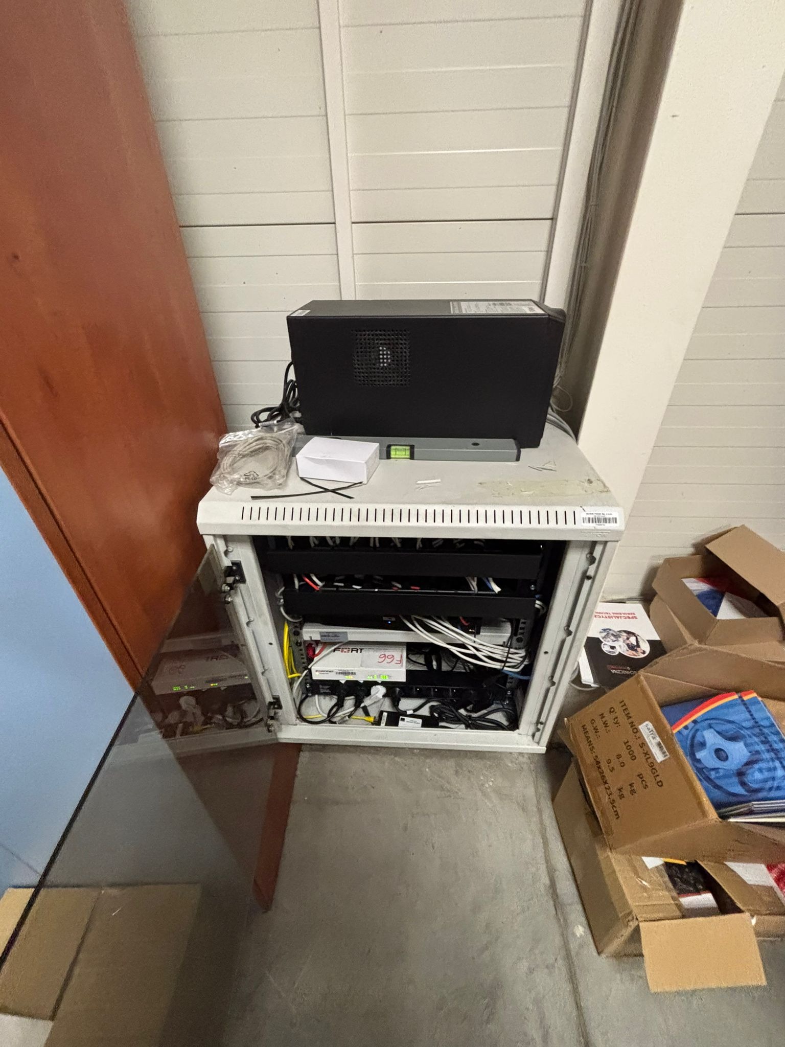 Szafa rack z zainstalowanymi urządzeniami sieciowymi i zasilaczem UPS na górze, widok z góry, obok kartony. Element sieci komputerowej w pomieszczeniu.