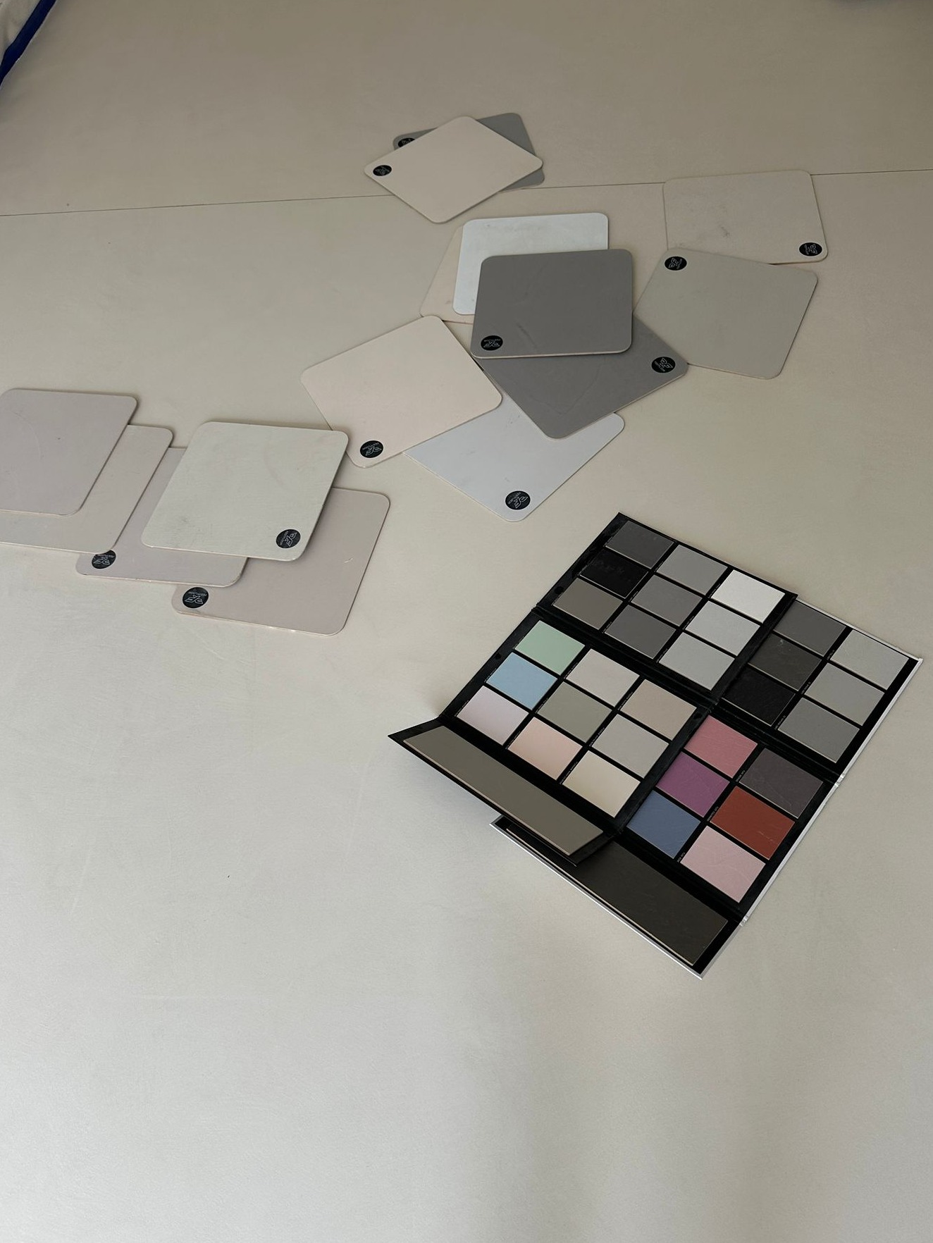 Paleta kolorów i próbki materiałów posadzkowych w odcieniach szarości i beżu, rozłożone na jasnej powierzchni. Wybór kolorystyki.