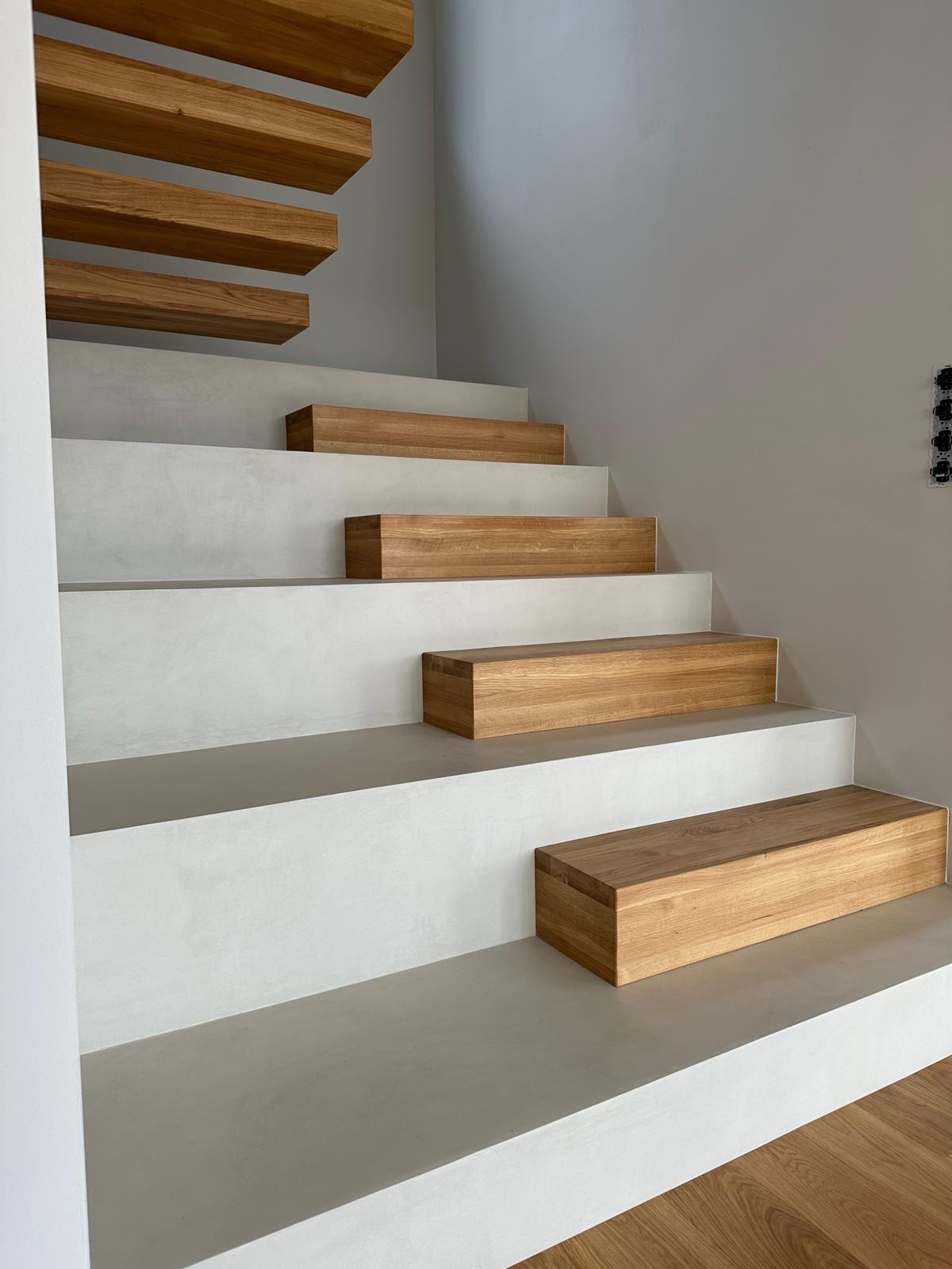 Nowoczesne schody z białego betonu i drewnianymi stopniami, minimalistyczny design, jasne wnętrze, widoczne detale wykończenia, gładka powierzchnia.