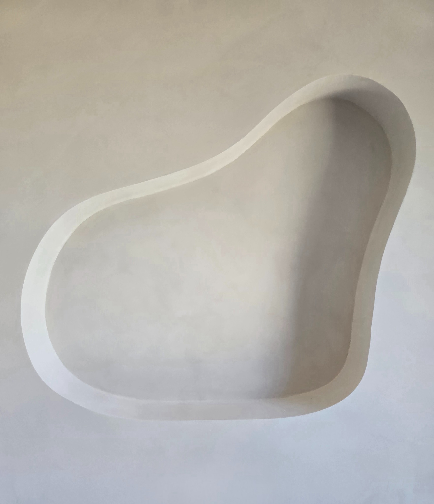 Nietypowa, wnęka w ścianie, wykończona w odcieniach bieli. Gładka powierzchnia, brak ostrych krawędzi, zaokrąglony kształt. Minimalistyczny design.