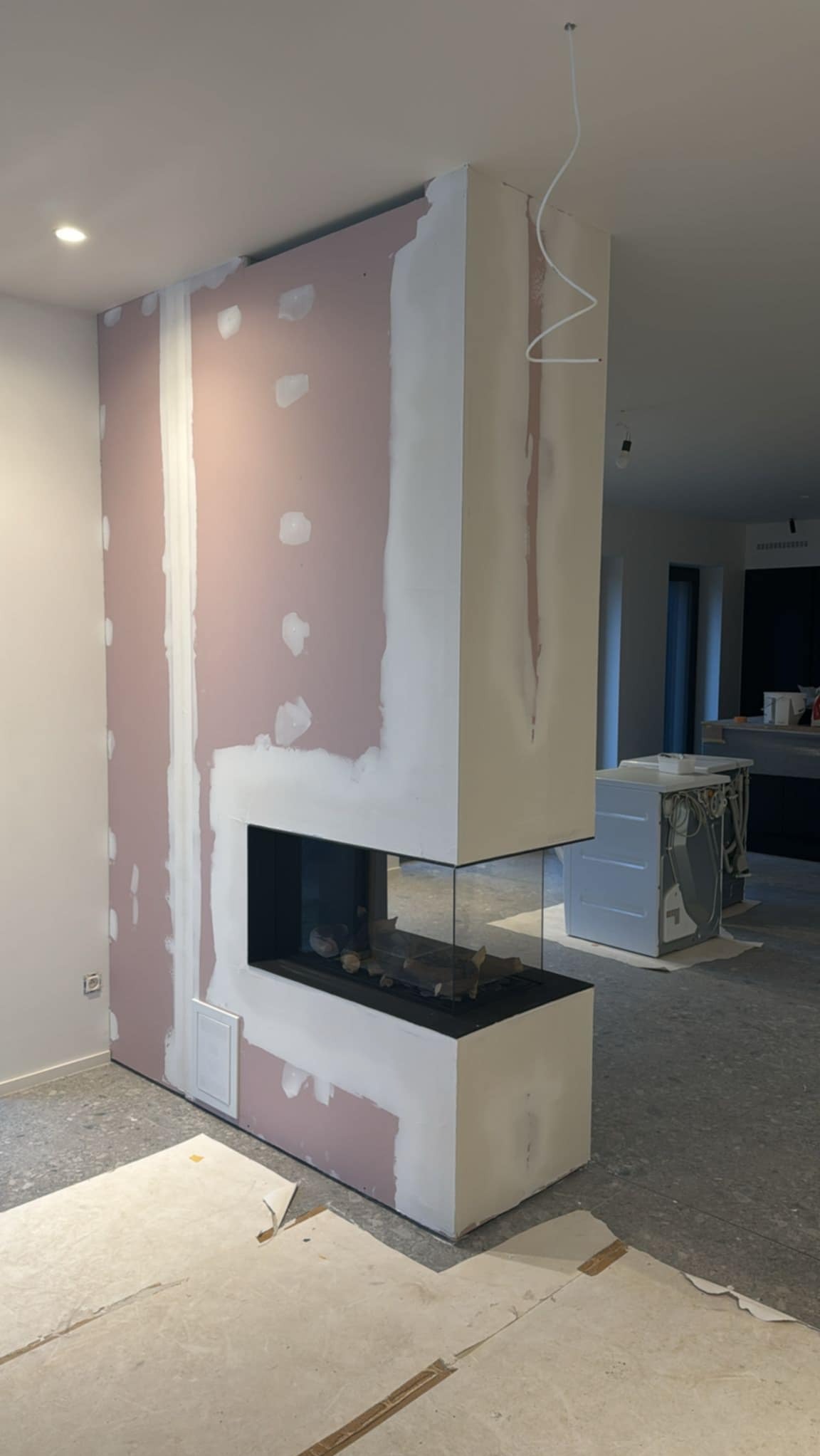 Wnętrze w trakcie prac wykończeniowych: obudowa kominka z płyt karton-gips, widoczne szpachlowanie i fragmenty niezabezpieczonej podłogi.