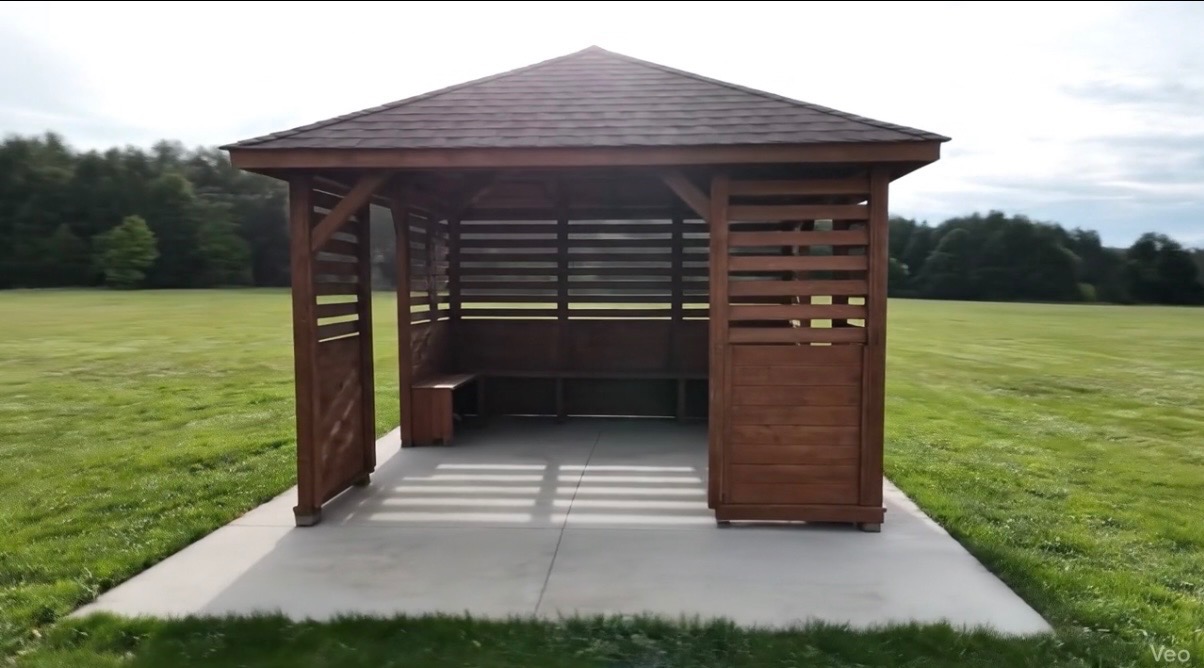 Drewniana altana z brązowym dachem na betonowej podstawie, otoczona zielonym trawnikiem i drzewami w tle. Widok z przodu, w słoneczny dzień.