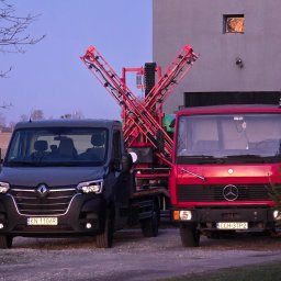 RKPOL Sp. z o.o. - Dwa samochody: szary Renault Master i czerwony Mercedes, z zamontowanym opryskiwaczem polowym, stoją na żwirowej drodze, na tle budynku i pola.
