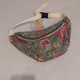 Pracownia Krawiecka - Atelier Marta Sierny-Kroczek - Saszetka nerka z motywem kwiatowym, leżąca na białym blacie. Widoczny pasek z klamrą i metka z logo Atelier Marta Słowy. Unikalny wzór i staranne wykonanie.