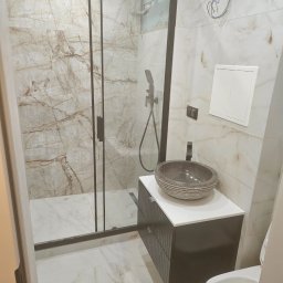 Remo-Bud - Nowoczesna łazienka z kabiną prysznicową typu walk-in, umywalką w stylu rustykalnym i marmurowymi płytkami ściennymi. Widoczne otwarte przewody elektryczne.