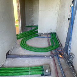 WIESŁAW SUSZEK USŁUGI WIELOBRANŻOWE - Zielone rury ogrzewania podłogowego ułożone w surowym wnętrzu, widoczne także rury instalacji wodnej w kolorach niebieskim i czerwonym. Etap prac przed wylaniem posadzki.