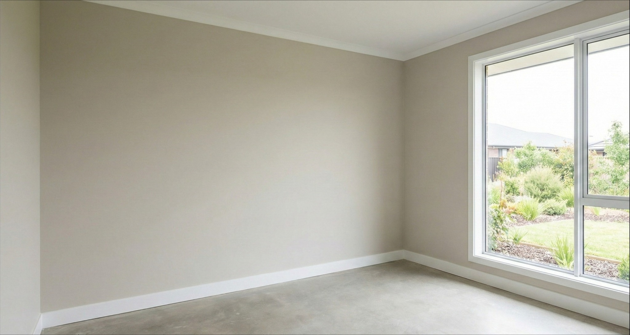 Jasne, puste wnętrze pokoju z beżowymi ścianami, białymi listwami przypodłogowymi i dużym oknem z widokiem na ogród. Minimalistyczny design, świeżo po malowaniu.
