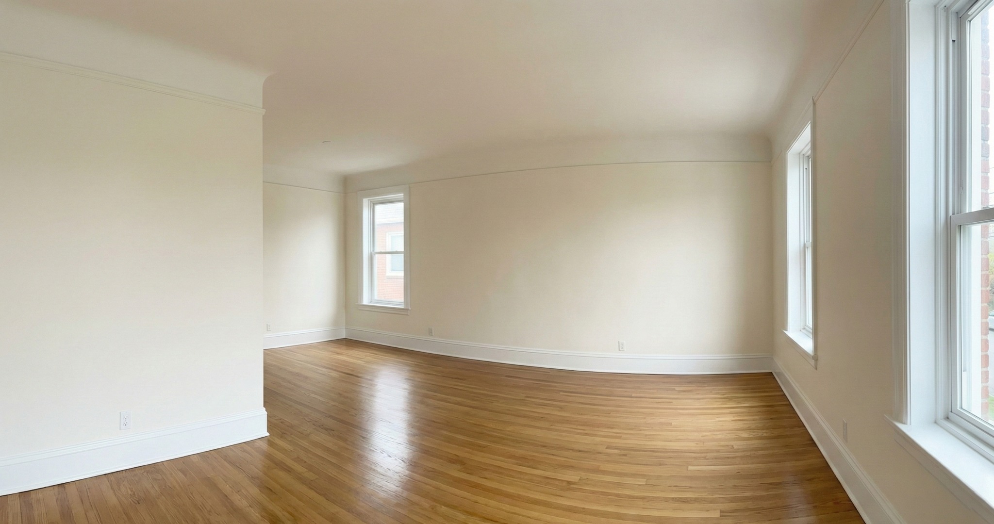Jasne, przestronne wnętrze po remoncie: świeżo pomalowane ściany w odcieniach bieli, parkiet w ciepłym odcieniu drewna, okna z białymi ramami. Minimalistyczny wystrój.