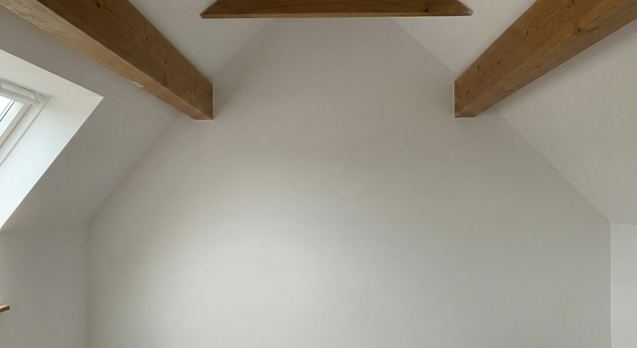 Białe, świeżo pomalowane poddasze w Zielonej Górze z drewnianymi belkami stropowymi i oknem dachowym. Minimalistyczny design, jasne wnętrze.