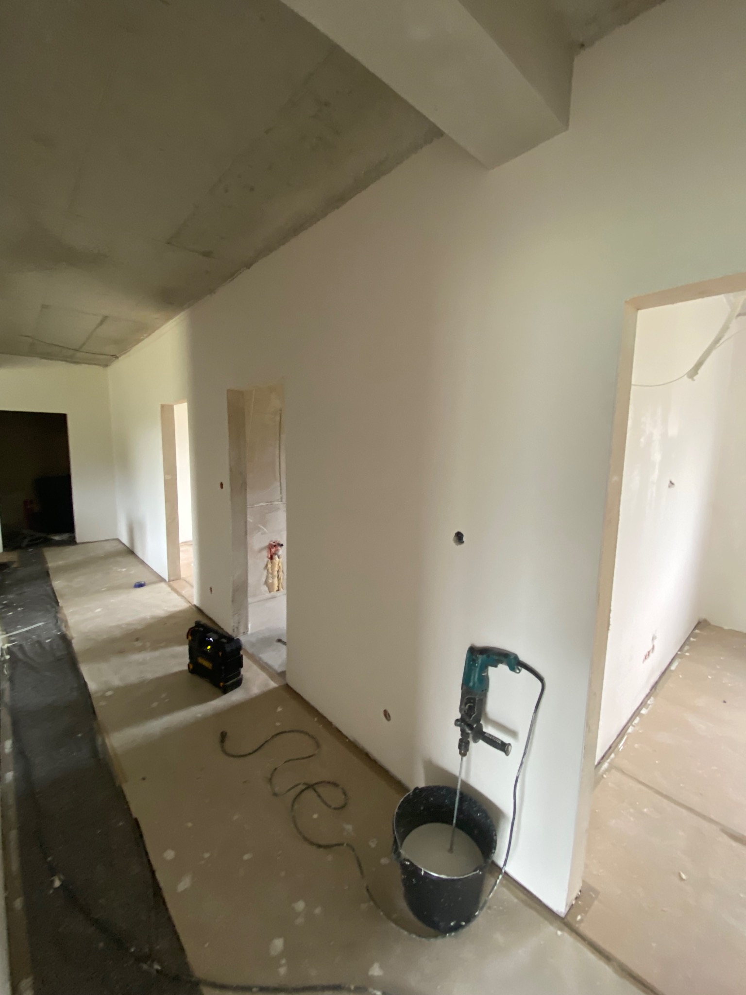 Wnętrze w trakcie prac wykończeniowych: ściany po szpachlowaniu, gotowe do malowania, mikser do gładzi w wiadrze, surowy sufit, przygotowane podłoże.