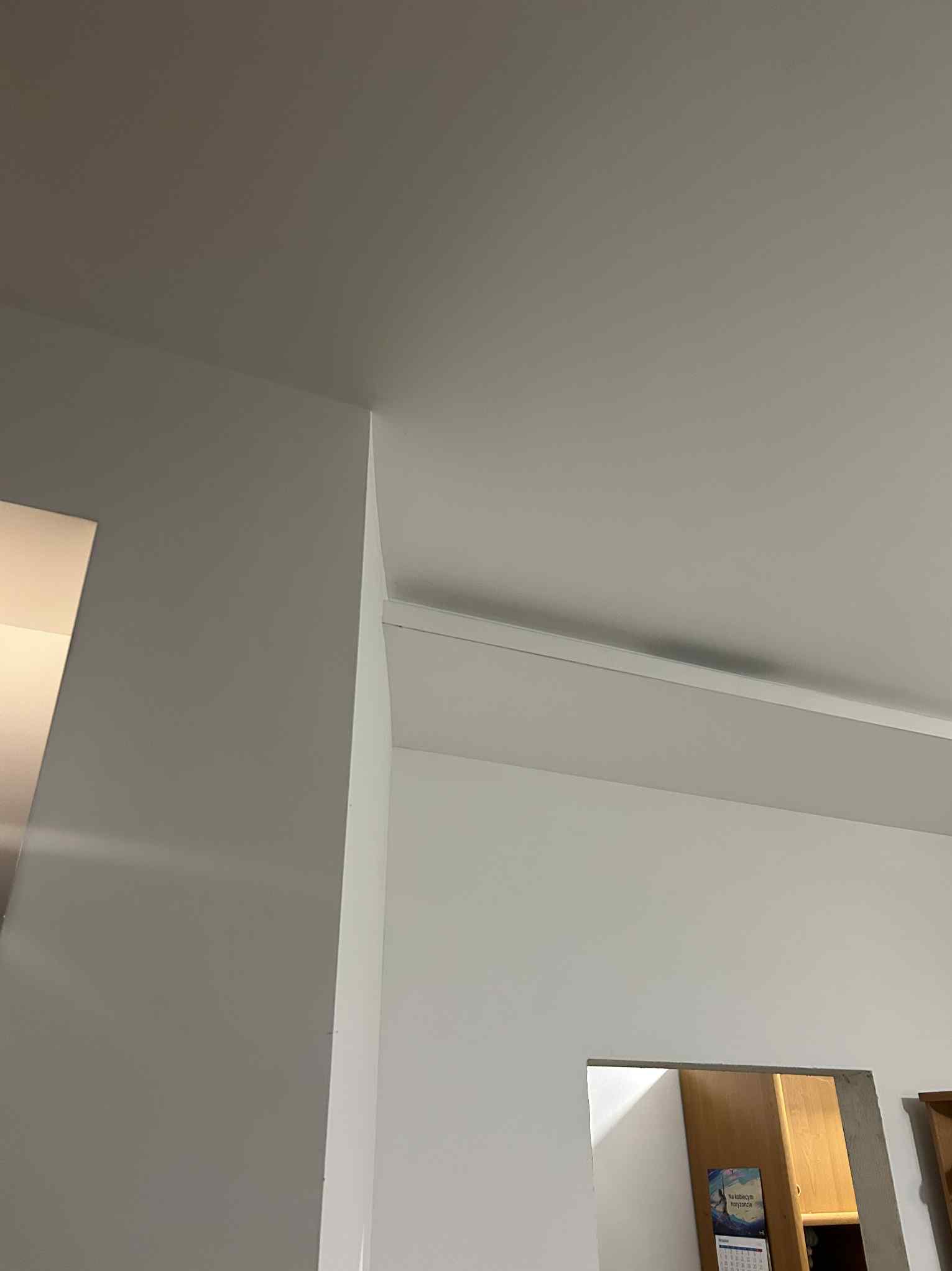 Ściana po szpachlowaniu i malowaniu na dwa kolory, z widocznym wykończeniem sufitu listwą przypodłogową. W tle fragment szafy i kalendarz.