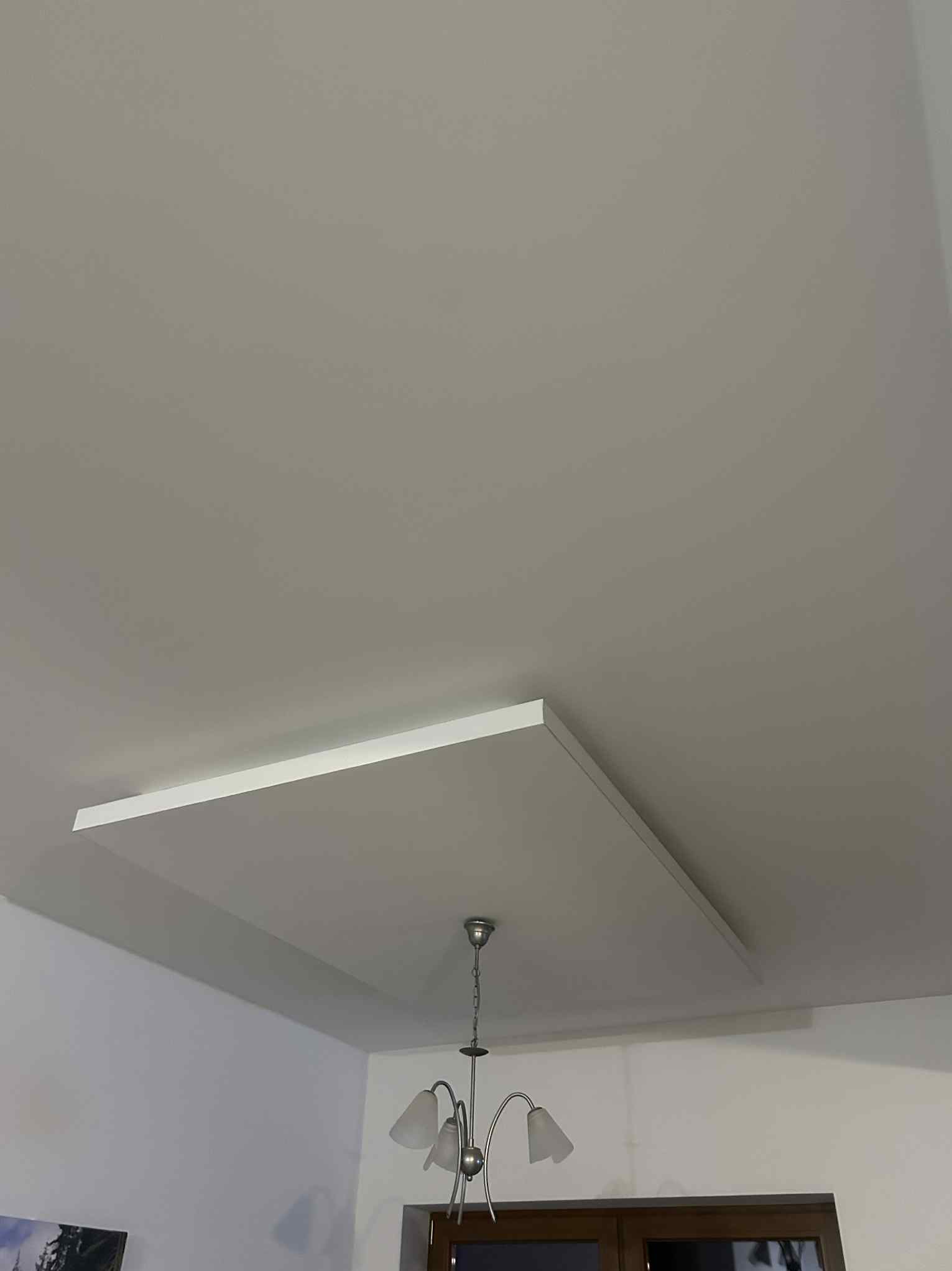 Wykończony sufit z płyt kartonowo-gipsowych z wbudowanym podwieszanym elementem w kształcie kwadratu i lampą wiszącą. Minimalistyczny design.