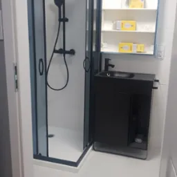 Nowoczesna, czarno-biała łazienka po remoncie: kabina prysznicowa z czarnymi ramami, szafka z umywalką i lustrem. Widoczne detale wykończenia.