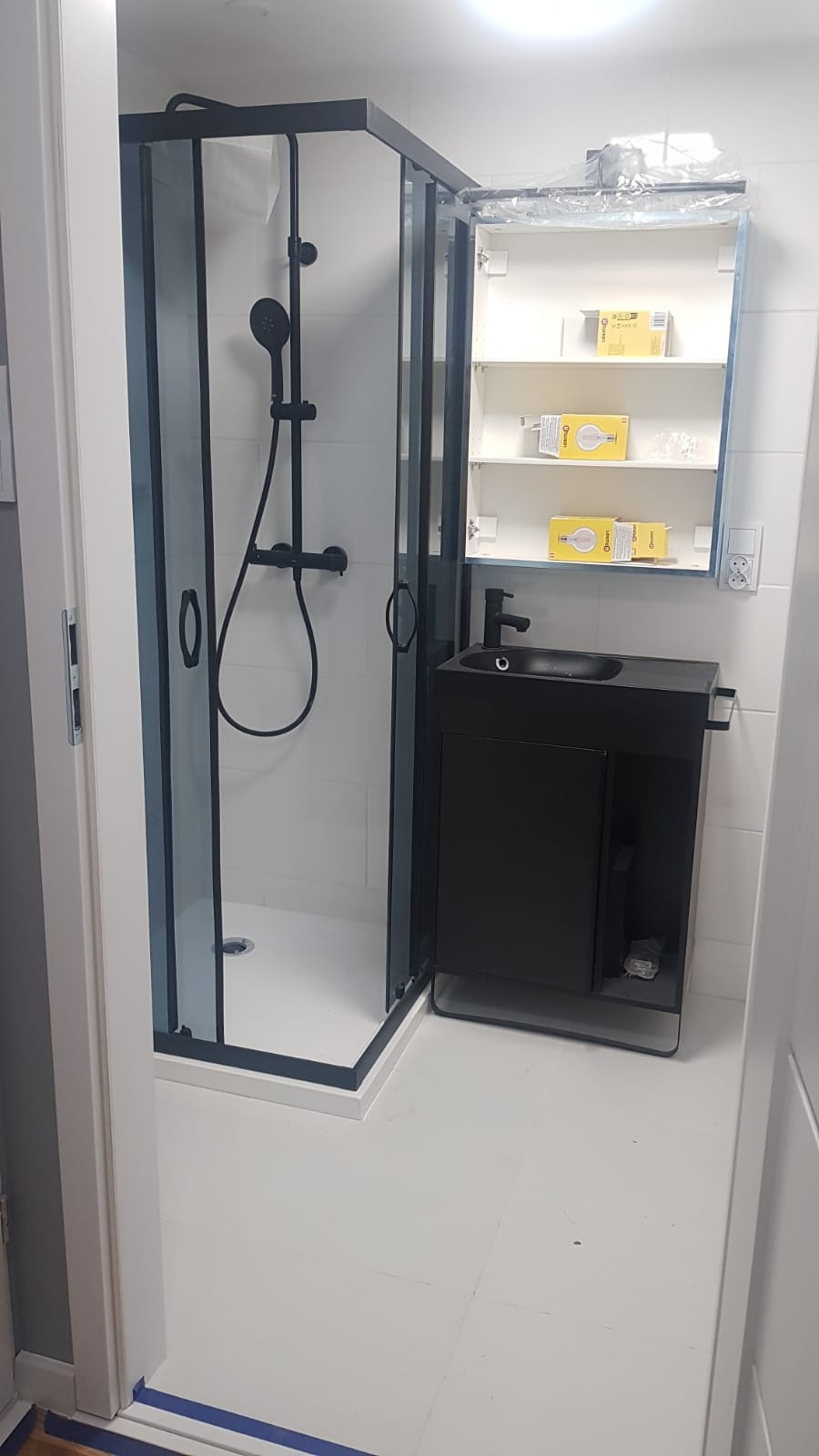 Nowoczesna, czarno-biała łazienka po remoncie: kabina prysznicowa z czarnymi ramami, szafka z umywalką i lustrem. Widoczne detale wykończenia.