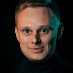 Portret mężczyzny z krótkimi blond włosami i niebieskimi oczami, ubranego w czarny golf, oświetlonego zielonkawym światłem z boku na ciemnym tle.