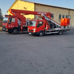 las bar Piotr Burda - Dwa czerwone podnośniki koszowe na tle budynku. Jeden MAN, drugi Nissan, oba z numerami telefonów. Jasne niebo, asfaltowy plac.