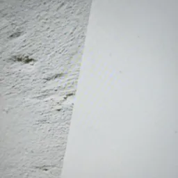 Fragment ściany: surowa faktura po lewej, gładka powierzchnia po prawej. Kontrast tekstur i odcieni szarości. Układ diagonalny.