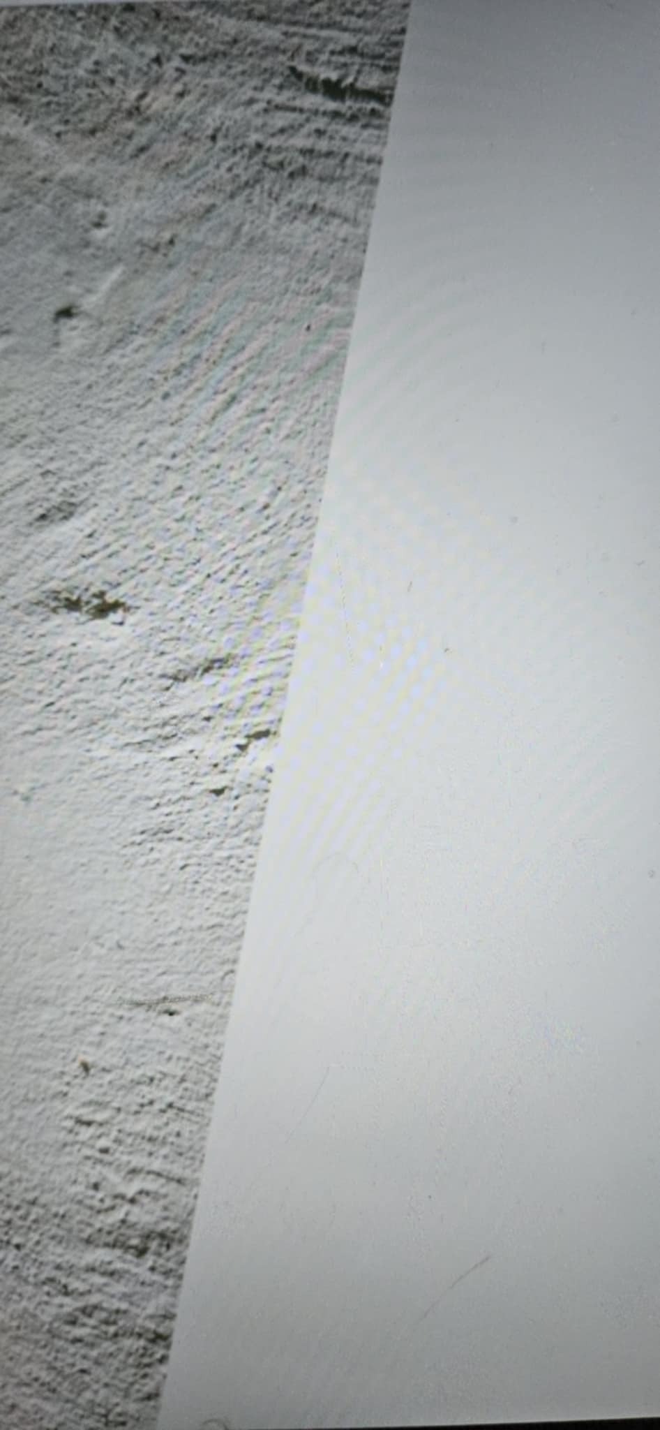 Fragment ściany: surowa faktura po lewej, gładka powierzchnia po prawej. Kontrast tekstur i odcieni szarości. Układ diagonalny.