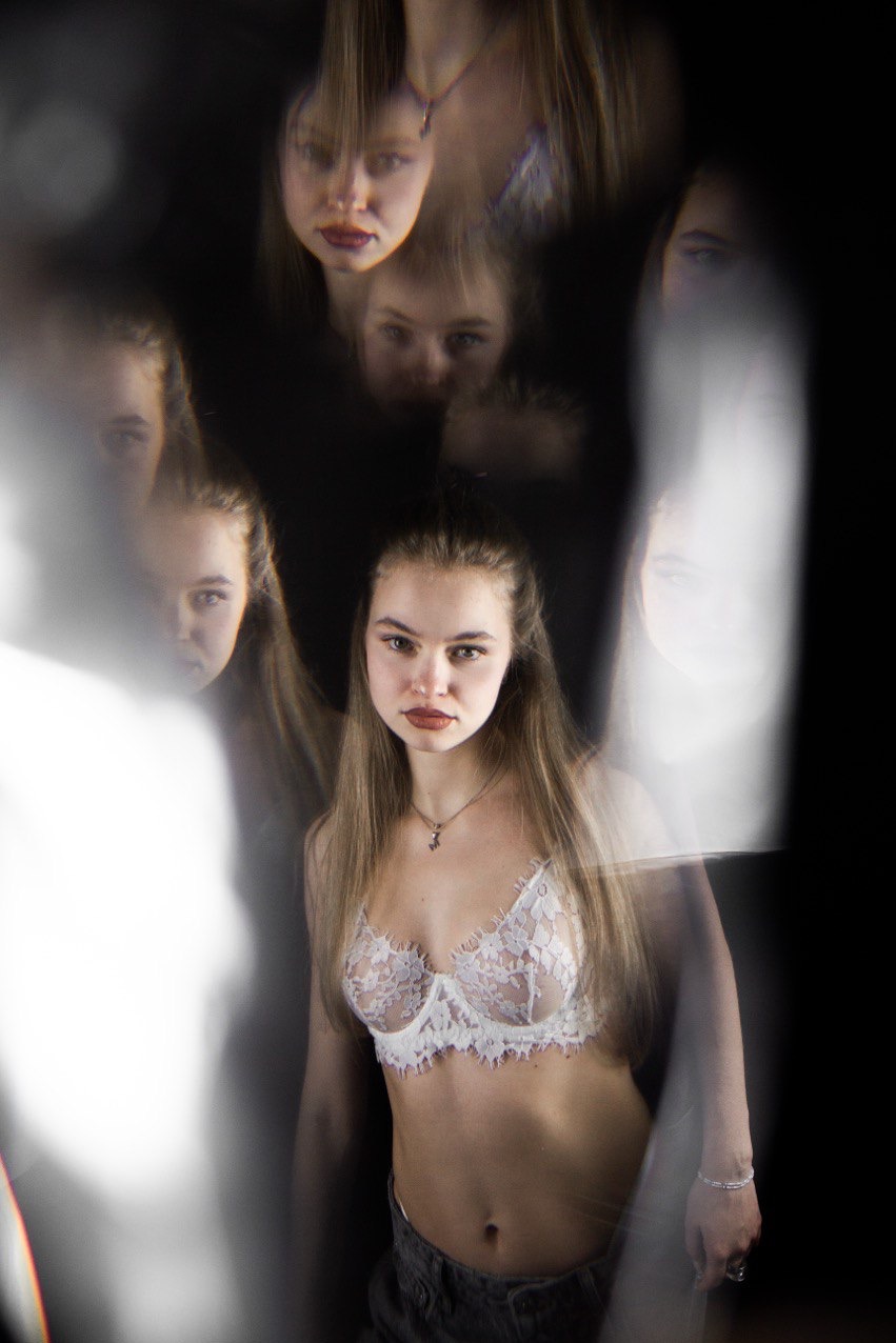 Portret młodej kobiety w bieliźnie na czarnym tle z efektem rozproszenia światła i odbić, tworzących artystyczny, niemal abstrakcyjny obraz.