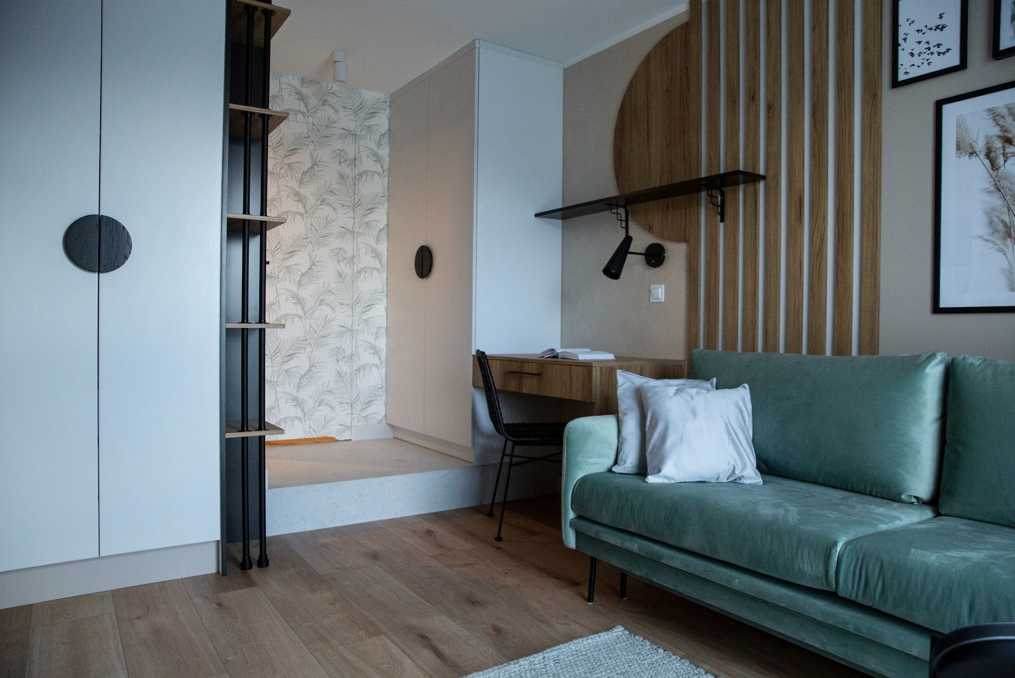 Nowoczesny pokój z zieloną sofą i biurkiem. Ściana z drewnianymi panelami i półką. Minimalistyczne oświetlenie i dekoracje. Parkiet na podłodze.