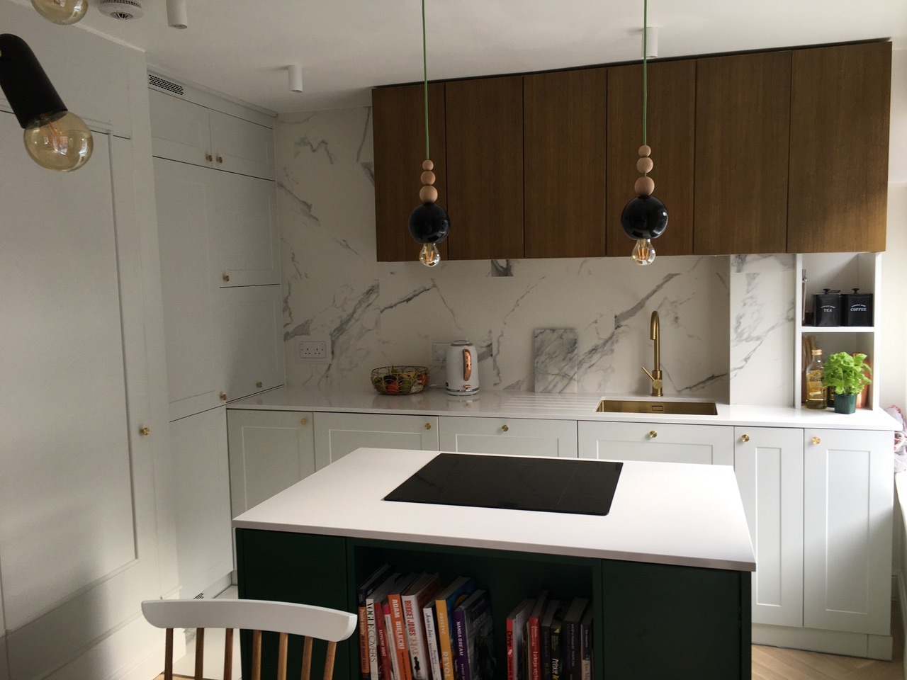 Nowoczesna kuchnia z wyspą, białe szafki z subtelnymi złotymi gałkami, marmurowy backsplash i drewniane szafki wiszące. Oświetlenie designerskie.