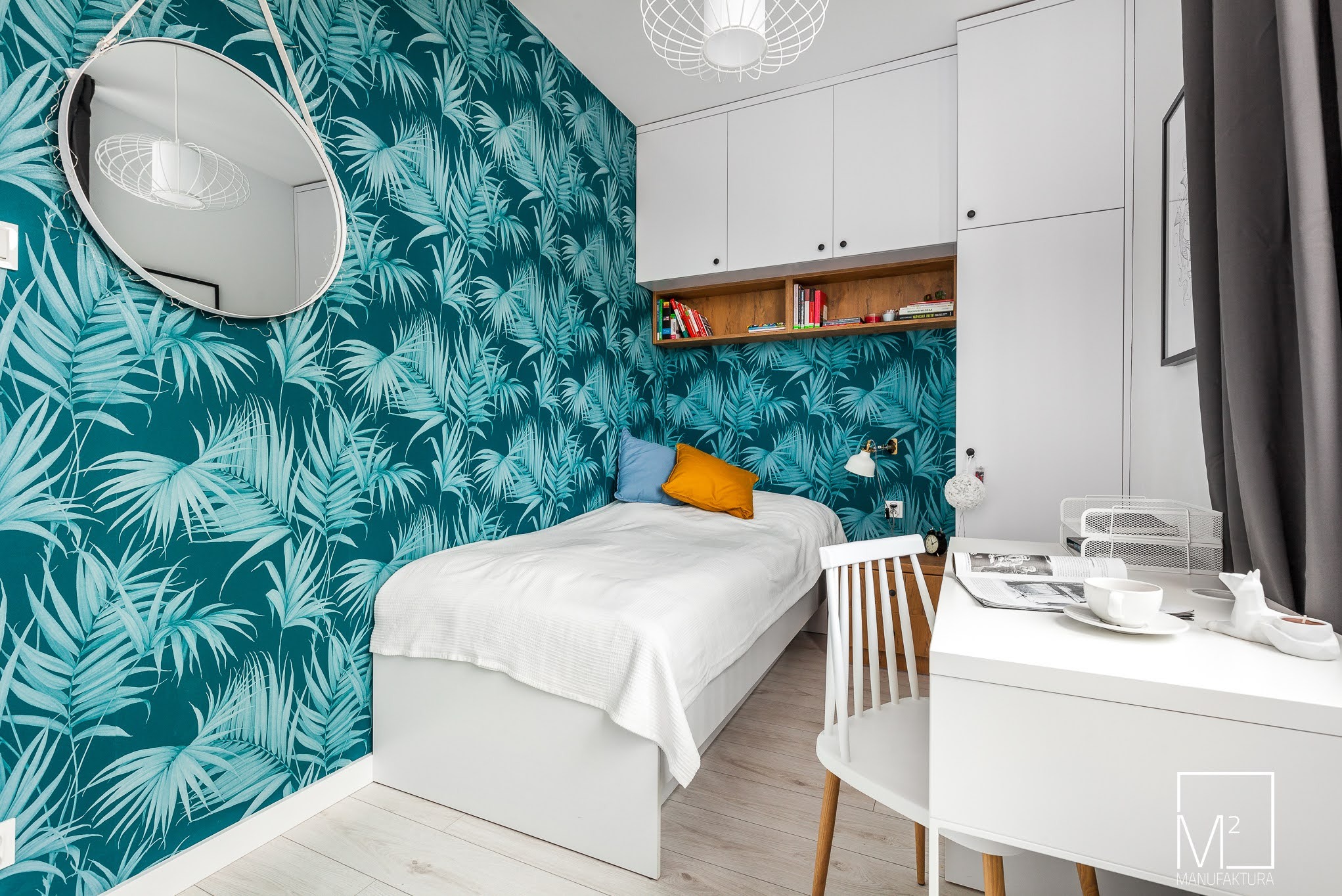 Pokój młodzieżowy z łóżkiem, biurkiem i szafkami w stylu skandynawskim. Turkusowa tapeta z motywem liści. Lustro na ścianie. Białe meble i drewniane podłogi.