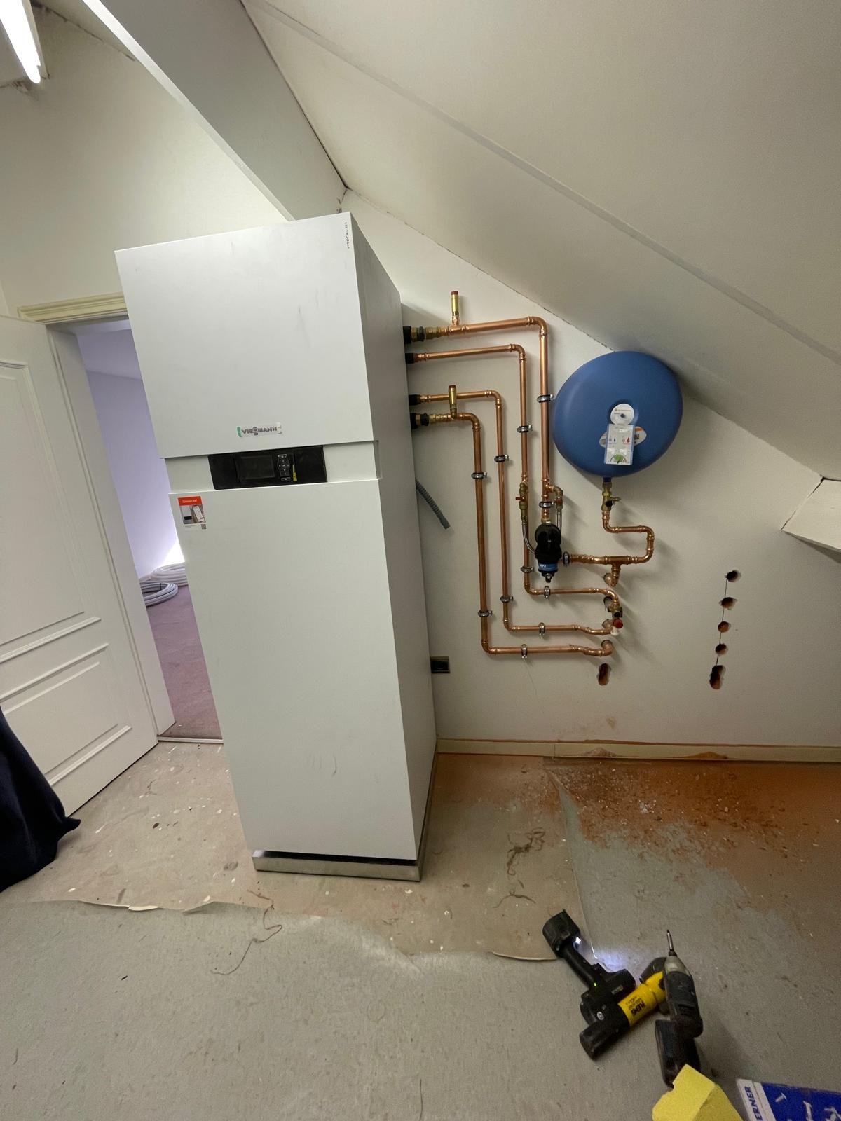 Nowoczesny piec gazowy Viessmann z miedzianą instalacją, zbiornikiem wyrównawczym i narzędziami na podłodze w trakcie montażu w pomieszczeniu na poddaszu.