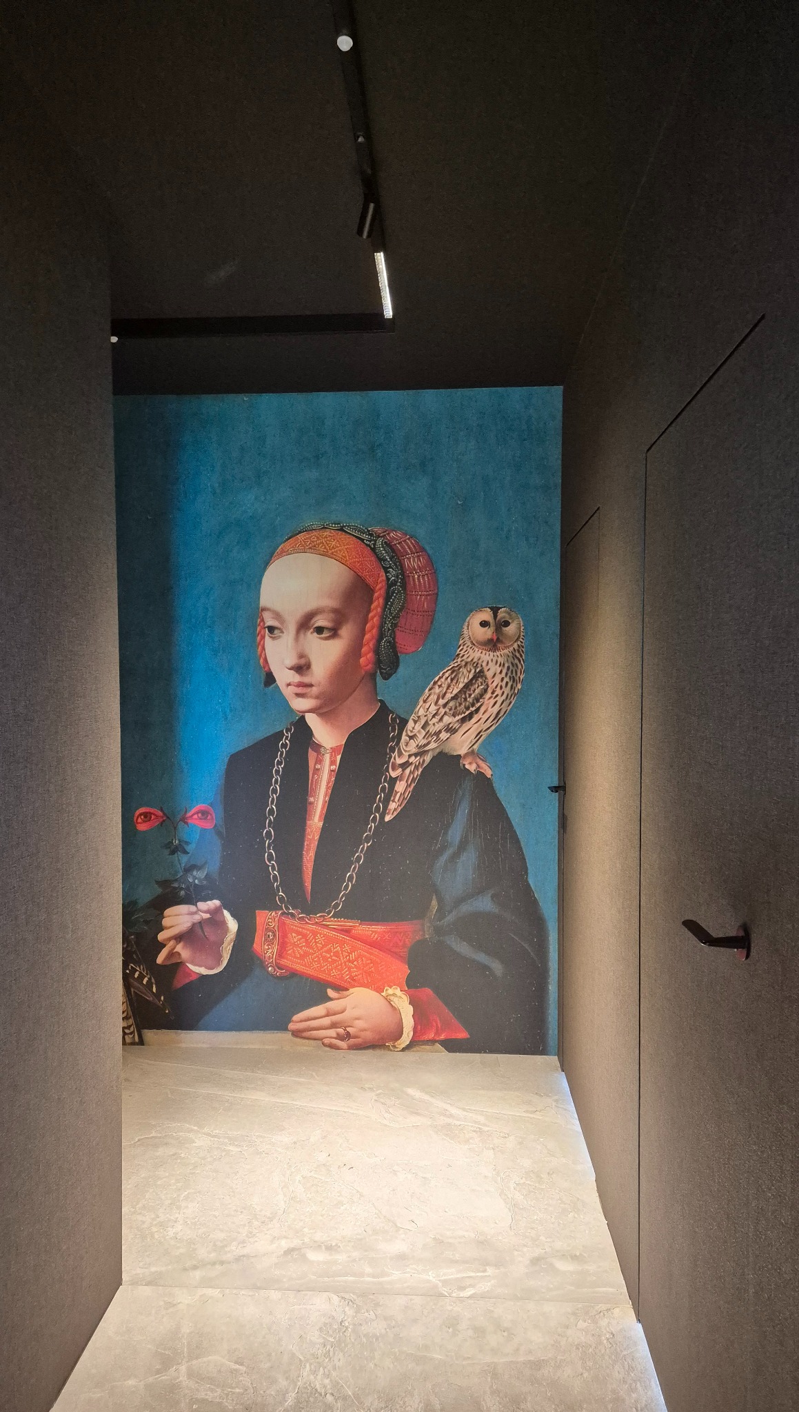 Tapeta z reprodukcją renesansowego portretu kobiety z sową, w korytarzu o minimalistycznym wystroju, z szarą podłogą i drzwiami.