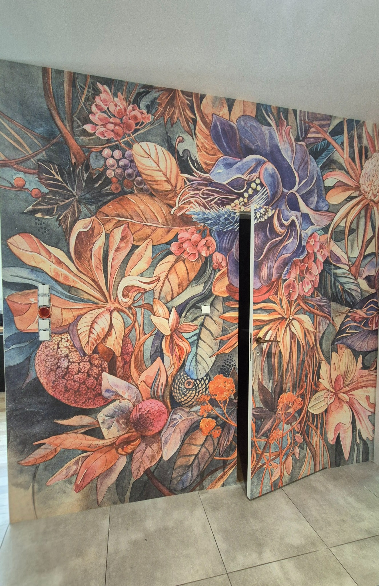 Ściana i drzwi pokryte fotorealistyczną tapetą z motywem kwiatowym w odcieniach brązu, niebieskiego i pomarańczu. Widoczne włączniki światła na ścianie.