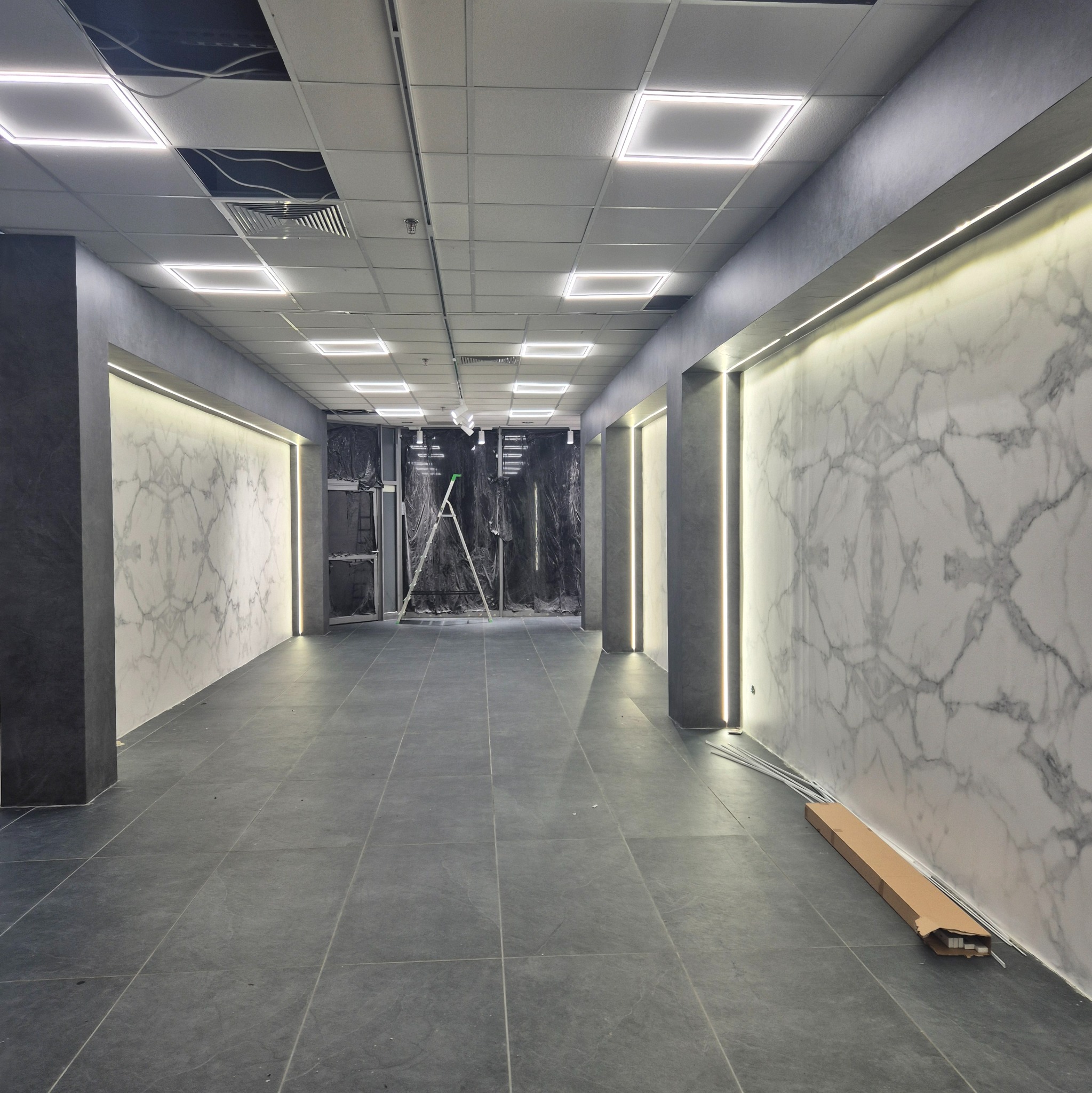 Wykończone wnętrze z marmurowymi ścianami i ledowym oświetleniem. Na podłodze szare płytki. Widoczna drabina i pozostałości po pracach wykończeniowych.