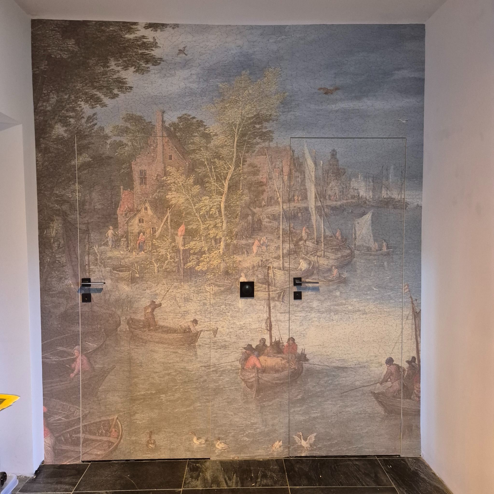 Ściana z fototapetą imitującą malarstwo holenderskie z motywem portu i łodzi, zintegrowana z dwiema parami drzwi z czarnymi klamkami.