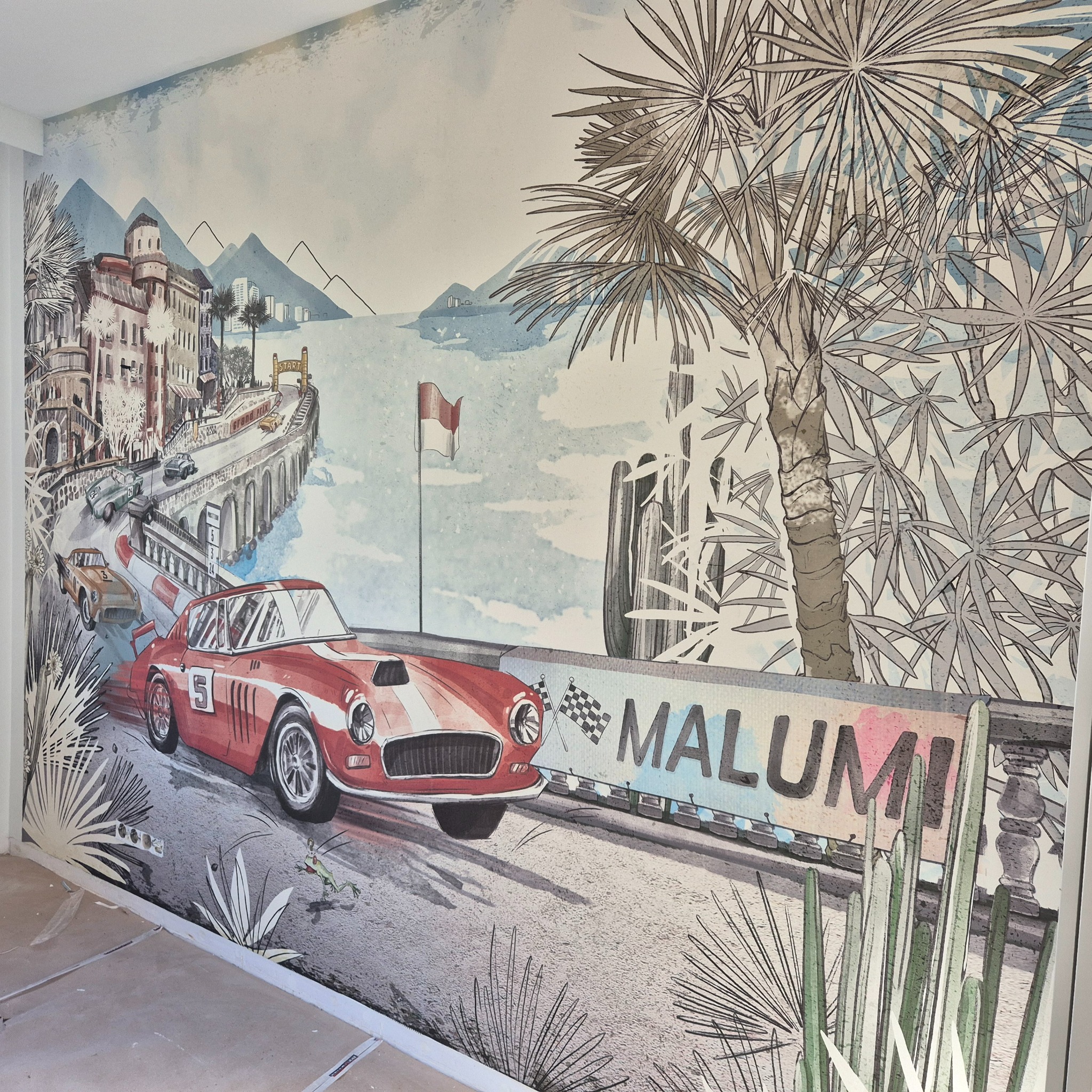 Ściana z tapetą przedstawiającą wyścigowy krajobraz Monte Carlo z czerwonym samochodem wyścigowym. Widoczny fragment podłogi w trakcie prac.