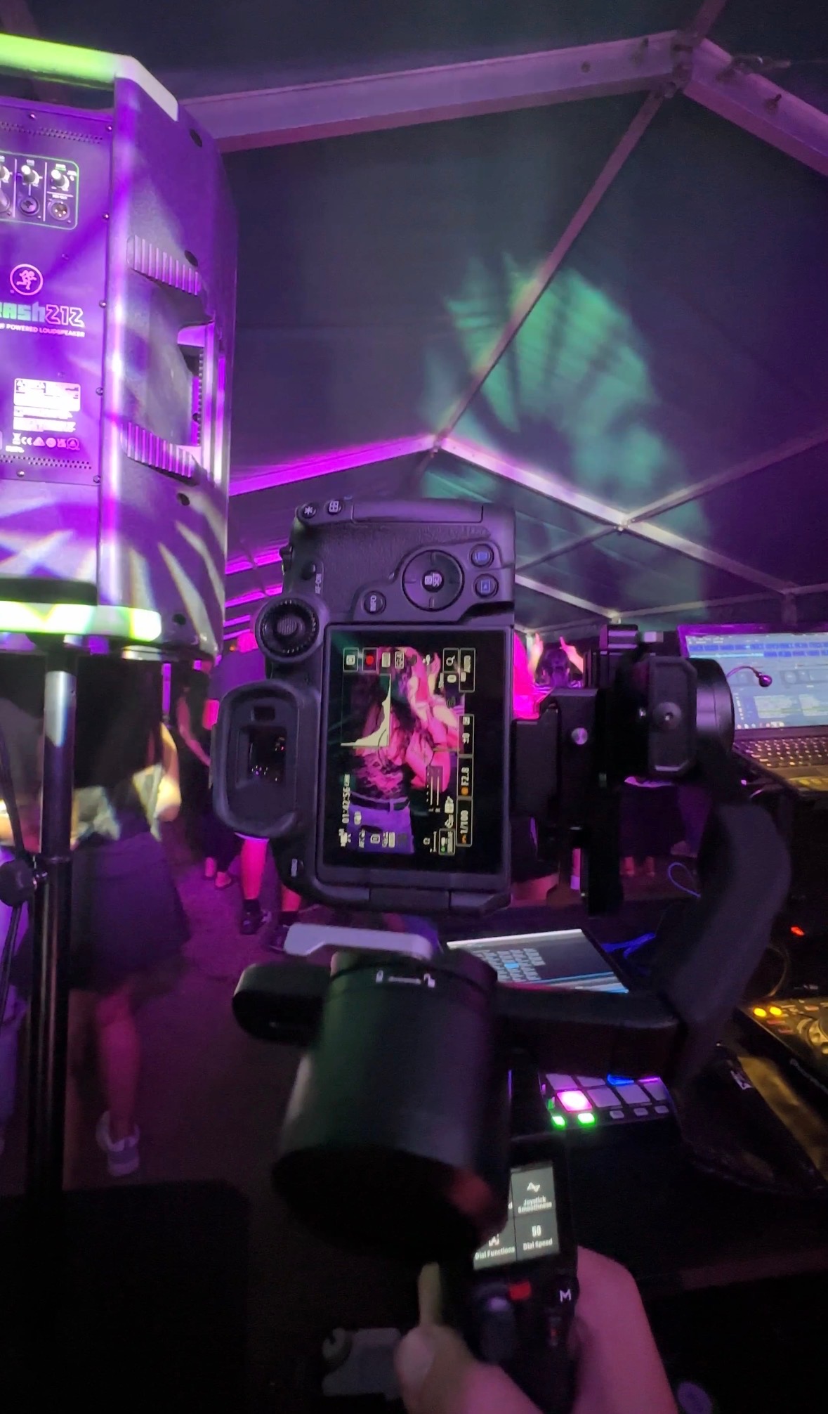 Kamera z podglądem nagrywanej osoby na tle sceny z oświetleniem eventowym i głośnikiem. Ujęcie z bliska na sprzęt podczas filmowania wydarzenia.