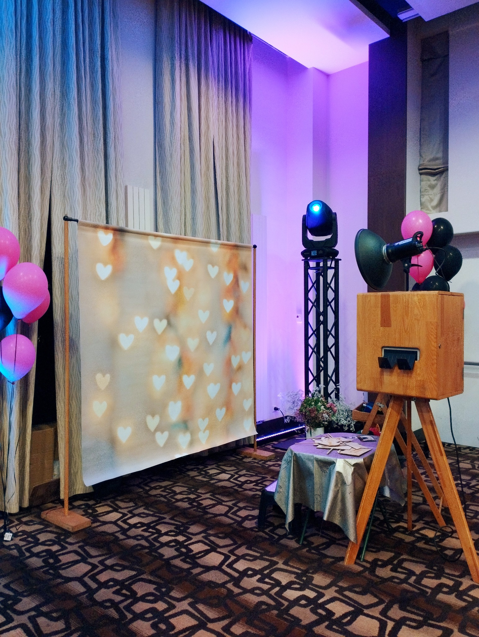 Drewniana fotobudka na trójnogu z tłem w serca i balonami, oświetlona fioletowym światłem, Sokołów Podlaski. Wyposażenie eventowe.