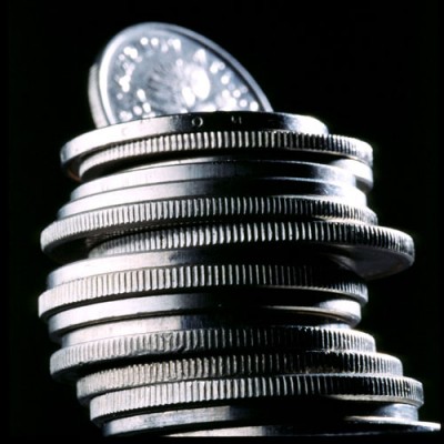 Stos srebrnych monet ułożonych jedna na drugiej na czarnym tle, z górną monetą wystającą ponad resztę.