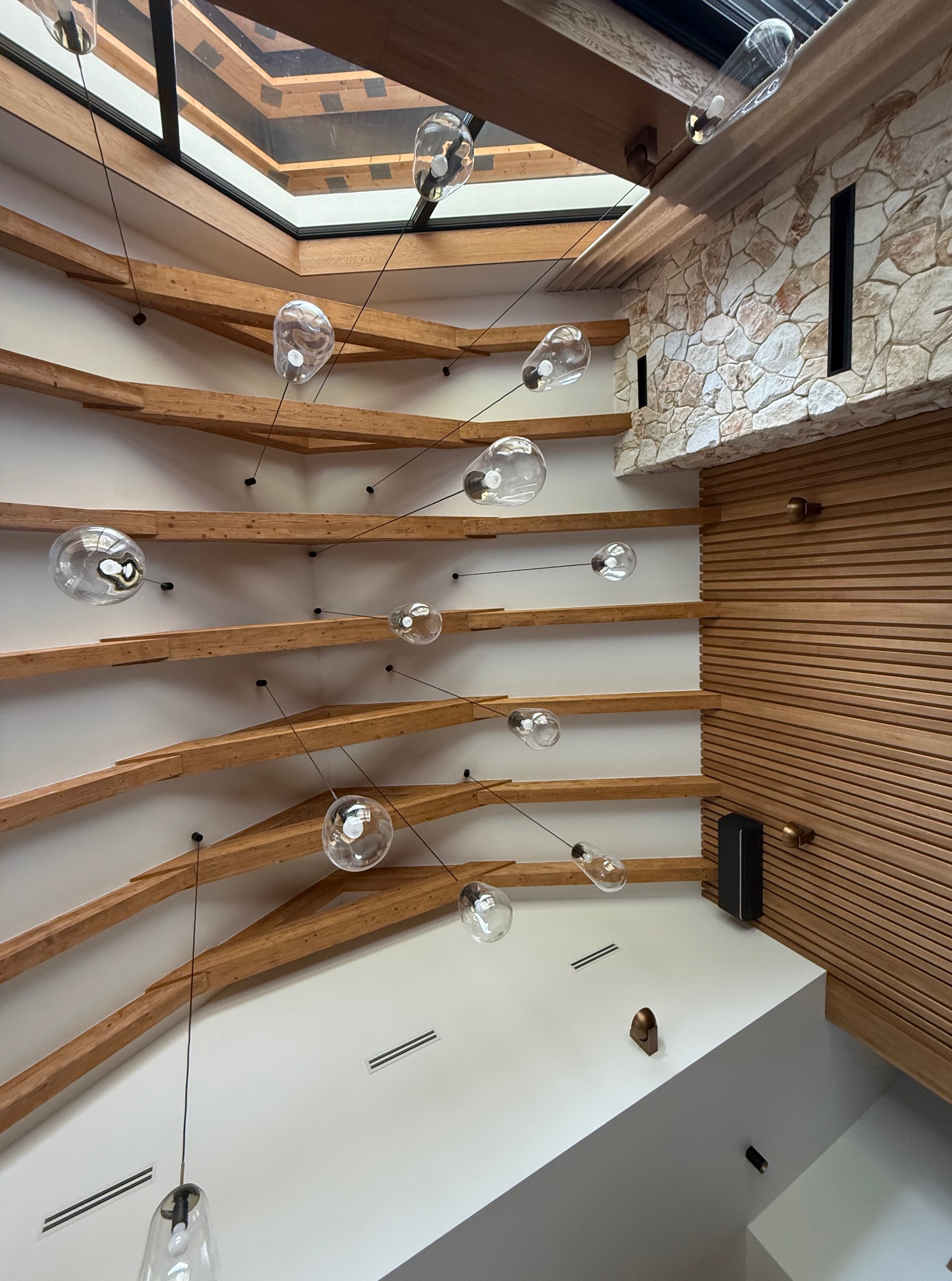 Nowoczesne wykończenie wnętrza z drewnianymi belkami sufitowymi, designerskim oświetleniem i elementami kamiennej ściany, widziane z perspektywy żabiej.
