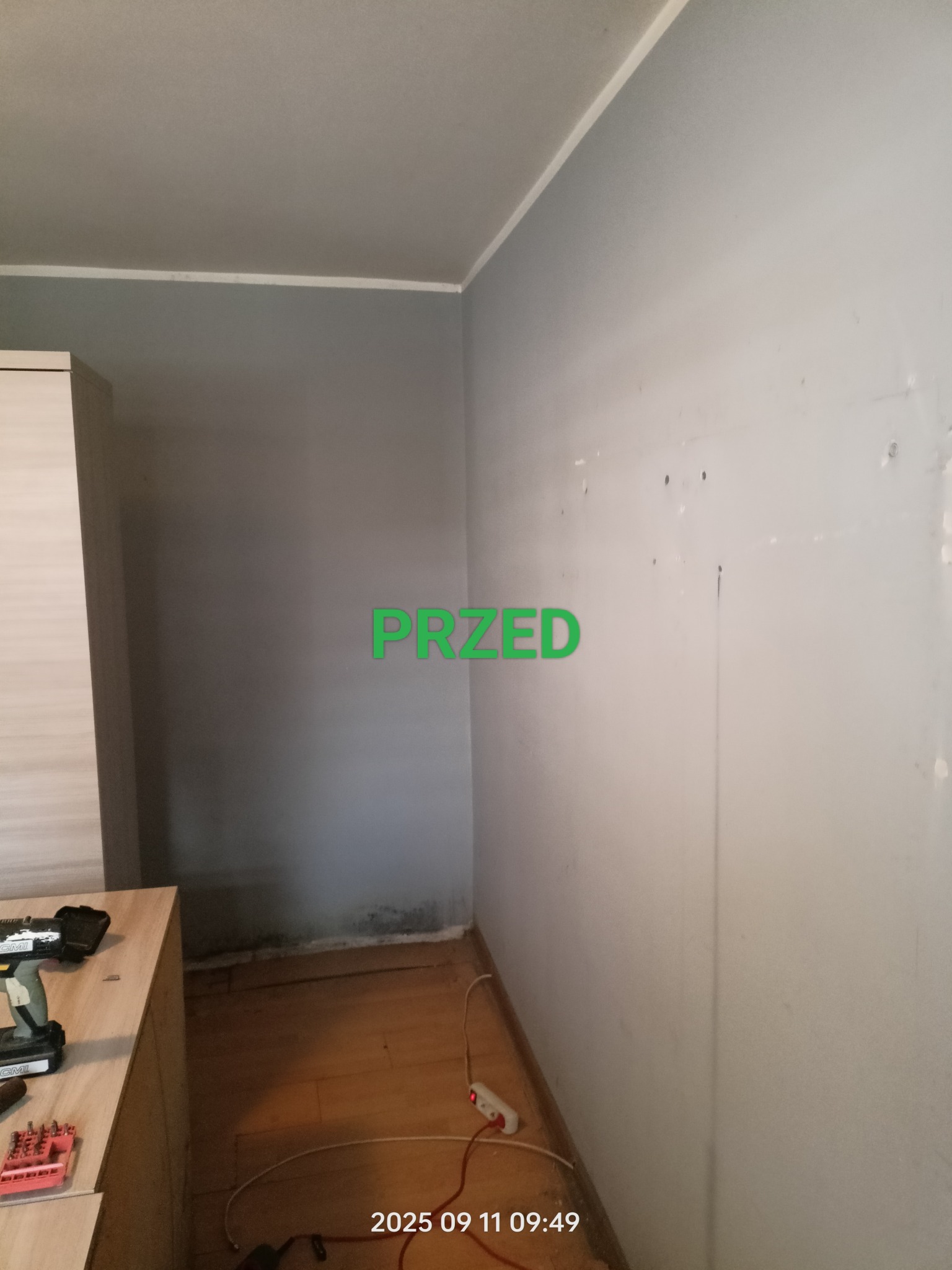 Pokój przed remontem: szara ściana z widocznymi śladami i zabrudzeniami, narzędzia na szafce, widoczny fragment podłogi. Napis 'PRZED' sugeruje etap prac.