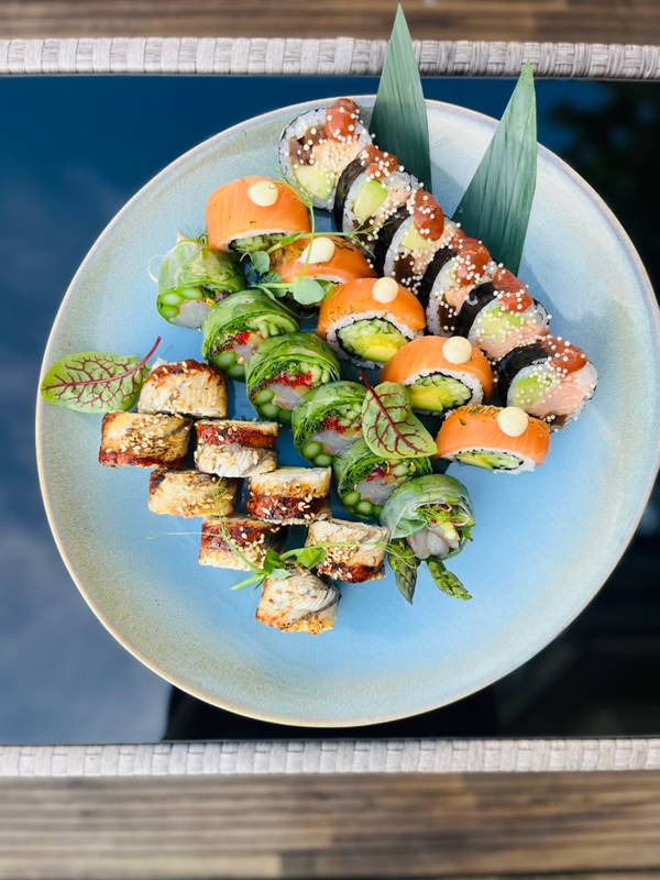 Dekoracyjny talerz z różnorodnymi sushi, w tym rolki z łososiem, awokado i węgorzem, ułożone na tle ciemnego stołu z drewnianym elementem w kadrze.