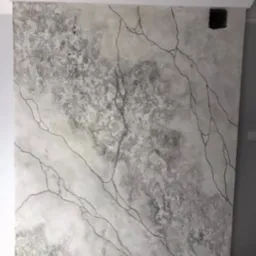 Ściana z efektem dekoracyjnym imitującym marmur z czarnymi żyłkami, widoczny otwór na gniazdko elektryczne, listwa przypodłogowa w dolnej części kadru.