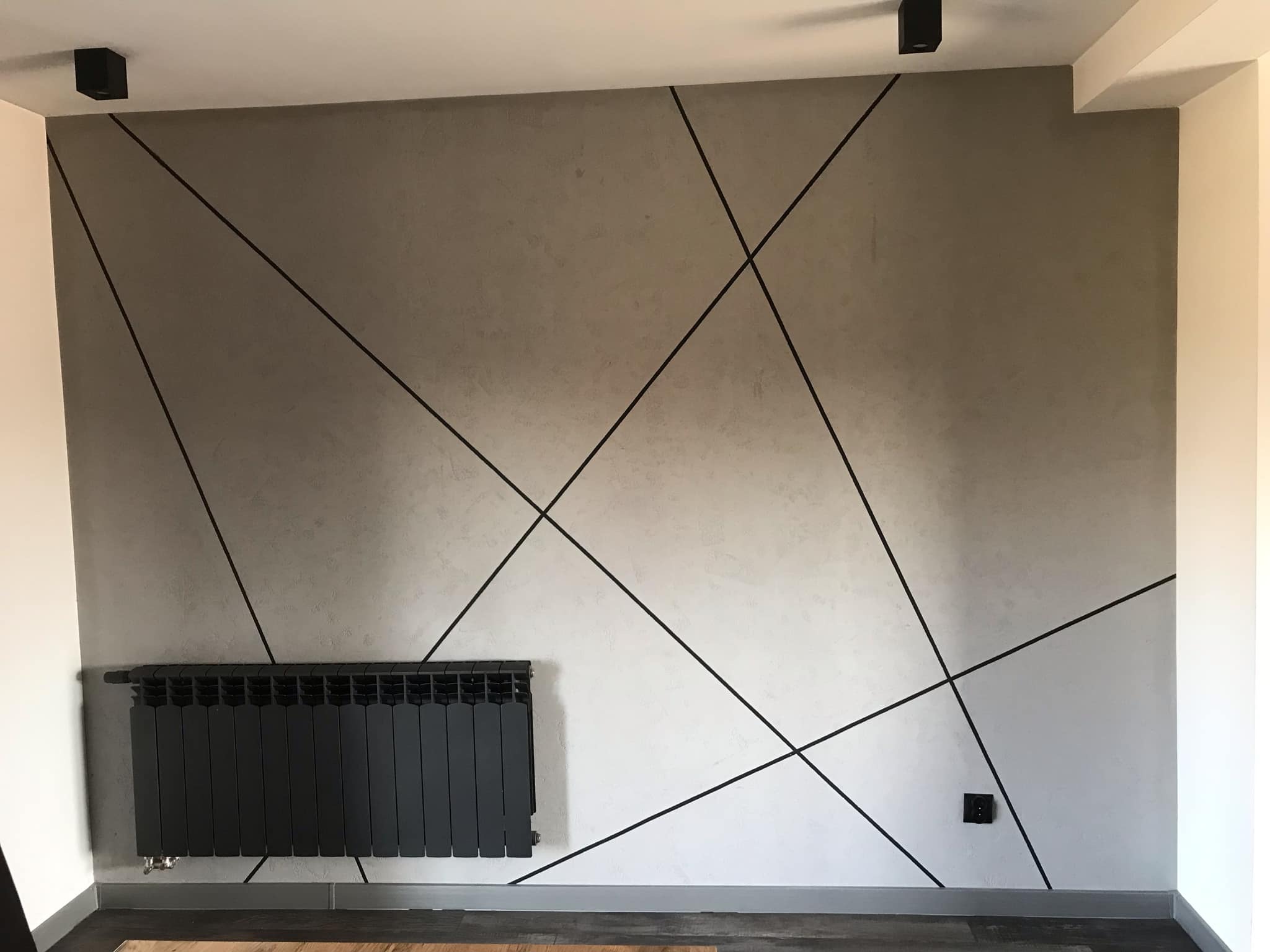 Wykończona ściana z dekoracyjnym wzorem z czarnych linii, szarym tynkiem strukturalnym i czarnym grzejnikiem. Minimalistyczny design wnętrza.