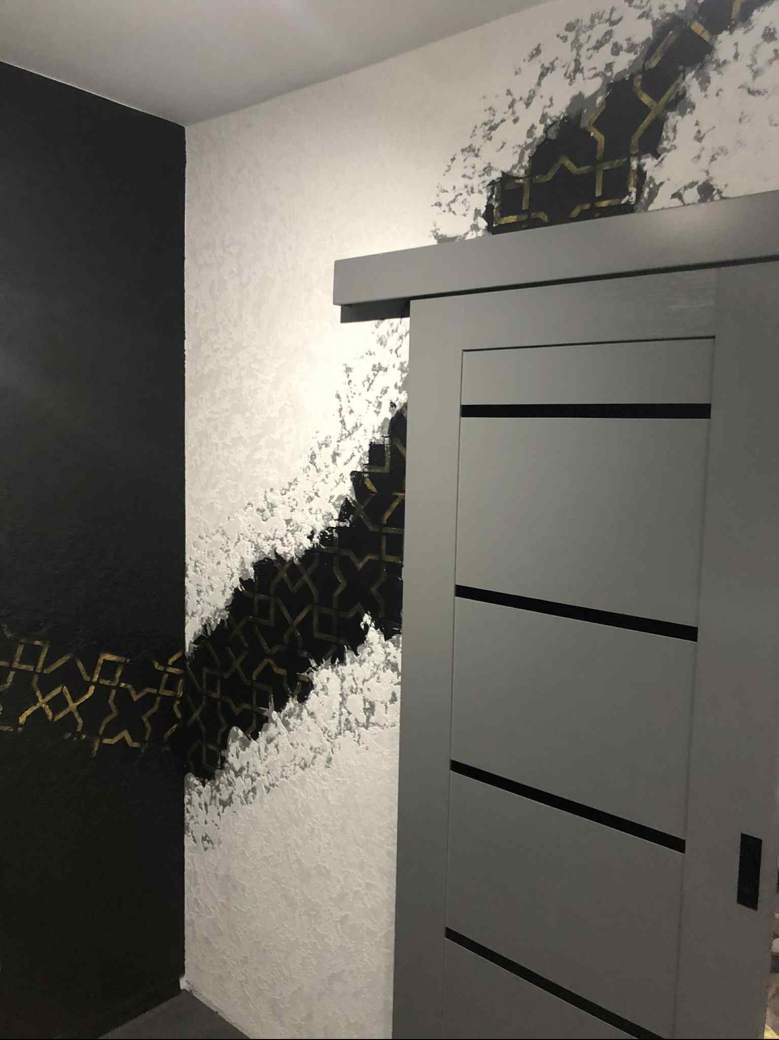 Nowoczesne malowanie ścian z efektem dekoracyjnym w czerni i bieli, złote geometryczne wzory, szare przesuwne drzwi. Oryginalne wykończenie wnętrza.