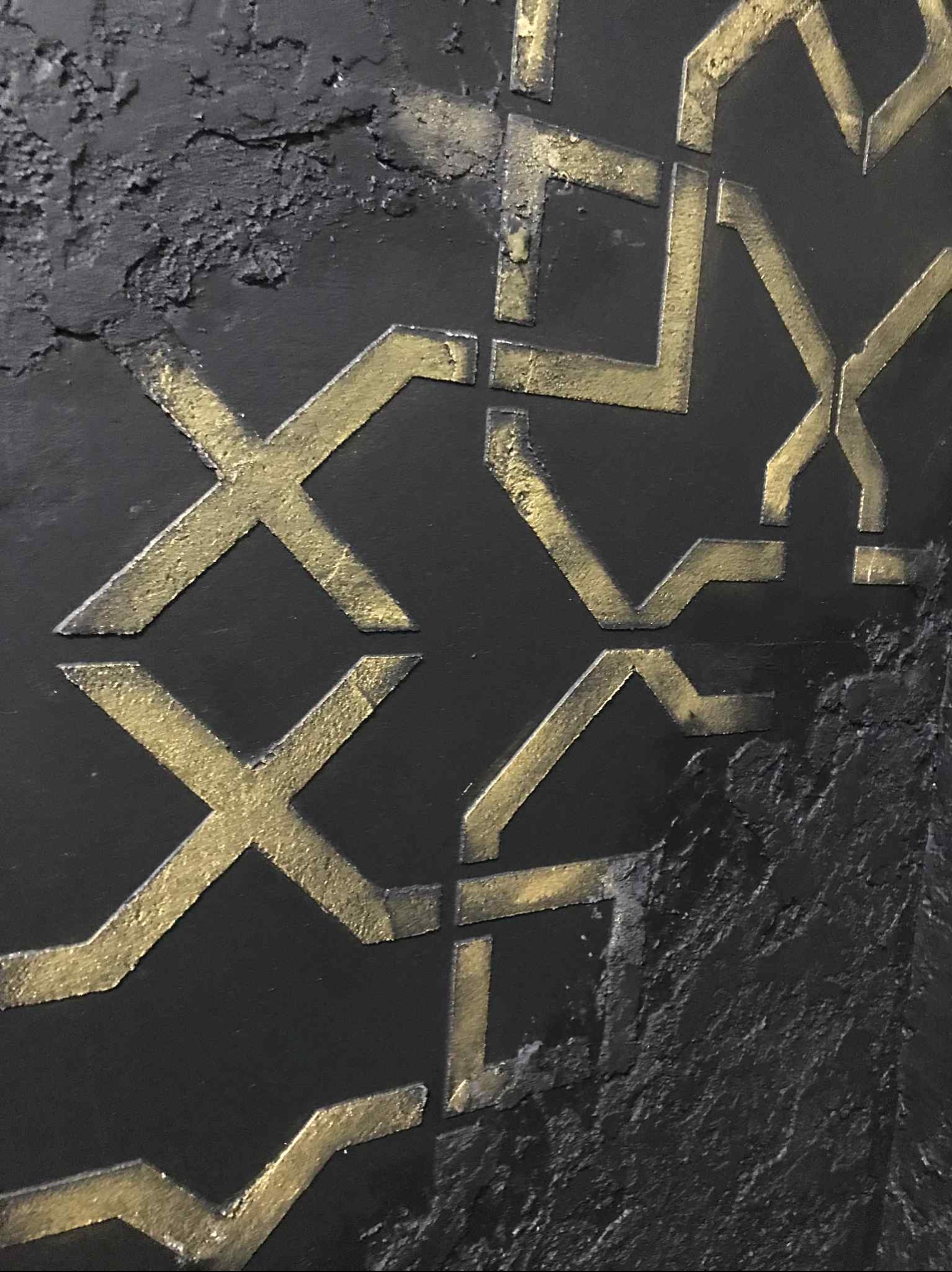 Czarno-złota dekoracyjna ściana z geometrycznym wzorem, wykonana z fakturą i metalicznym połyskiem. Detal wykończenia wnętrza z bliska.
