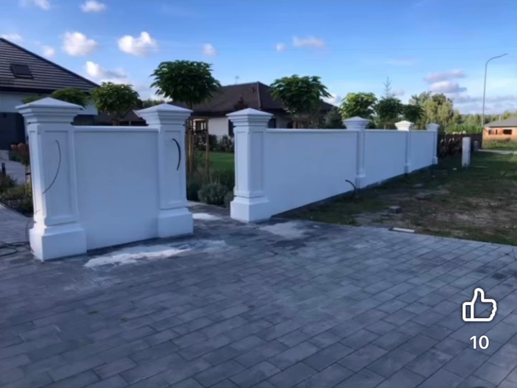 Biały, otynkowany mur z kolumnami na posesji, widok z brukowanego podjazdu. Błękitne niebo w tle. Estetyczne wykończenie.