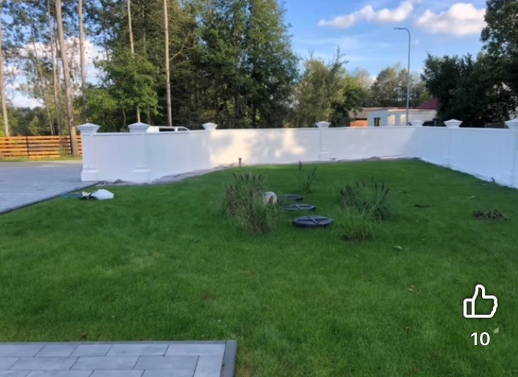 Biały, pomalowany mur z dekoracyjnymi słupkami na tle zielonego trawnika i drzew. Widoczne ślady po malowaniu, sugerujące świeżo wykonaną usługę.