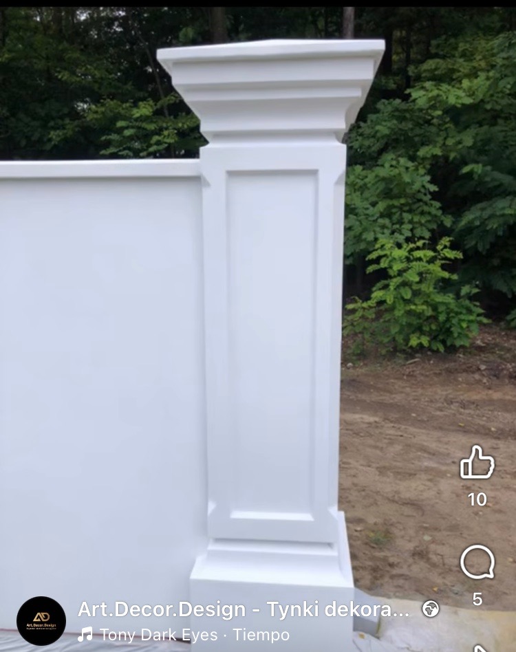 Biały, dekoracyjny filar z płyty karton-gips, imitujący kolumnę, na tle zieleni. Detal wykończenia z precyzyjnymi zdobieniami.