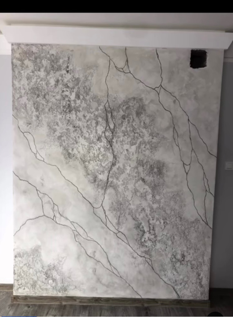 Ściana z efektem dekoracyjnym imitującym marmur z czarnymi żyłkami, widoczny otwór na gniazdko elektryczne, listwa przypodłogowa w dolnej części kadru.