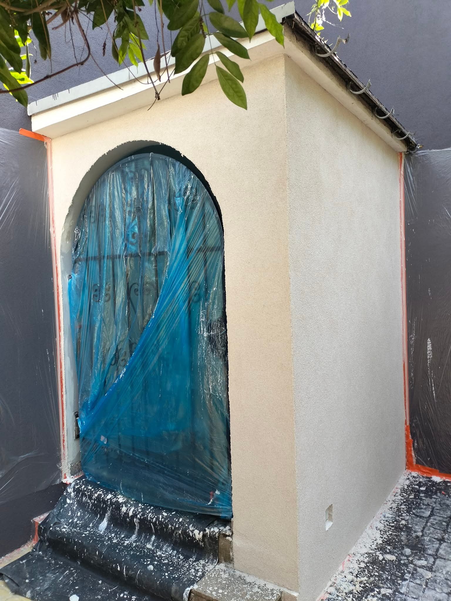 Otynkowane wejście z łukiem, zabezpieczone folią. Świeżo nałożony tynk na ścianie, widoczne ślady prac wykończeniowych. Zabezpieczone otoczenie.