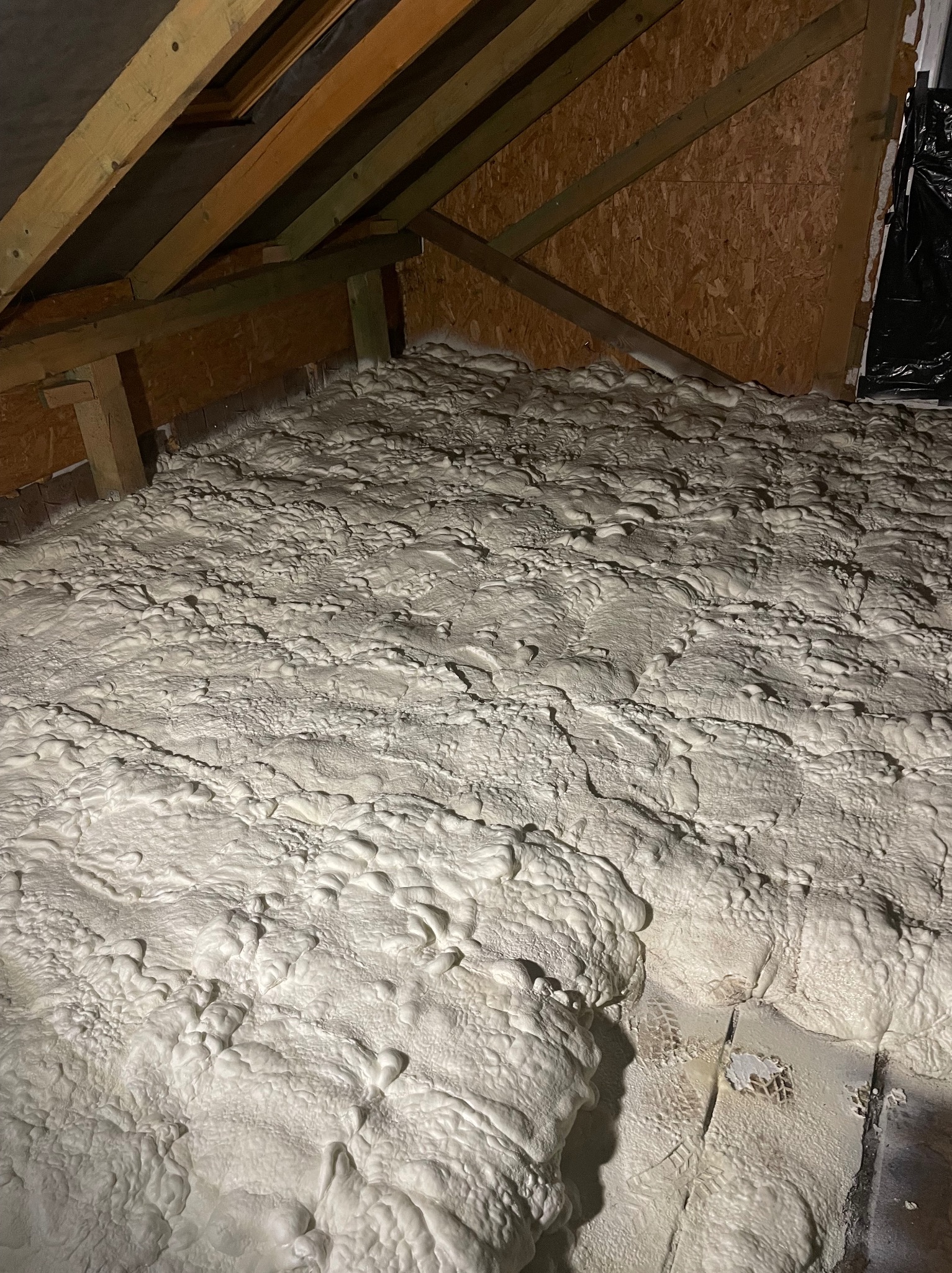 Poddasze po aplikacji pianki PUR, widoczne drewniane elementy konstrukcyjne dachu i warstwa izolacji. Charakterystyczna struktura pianki.